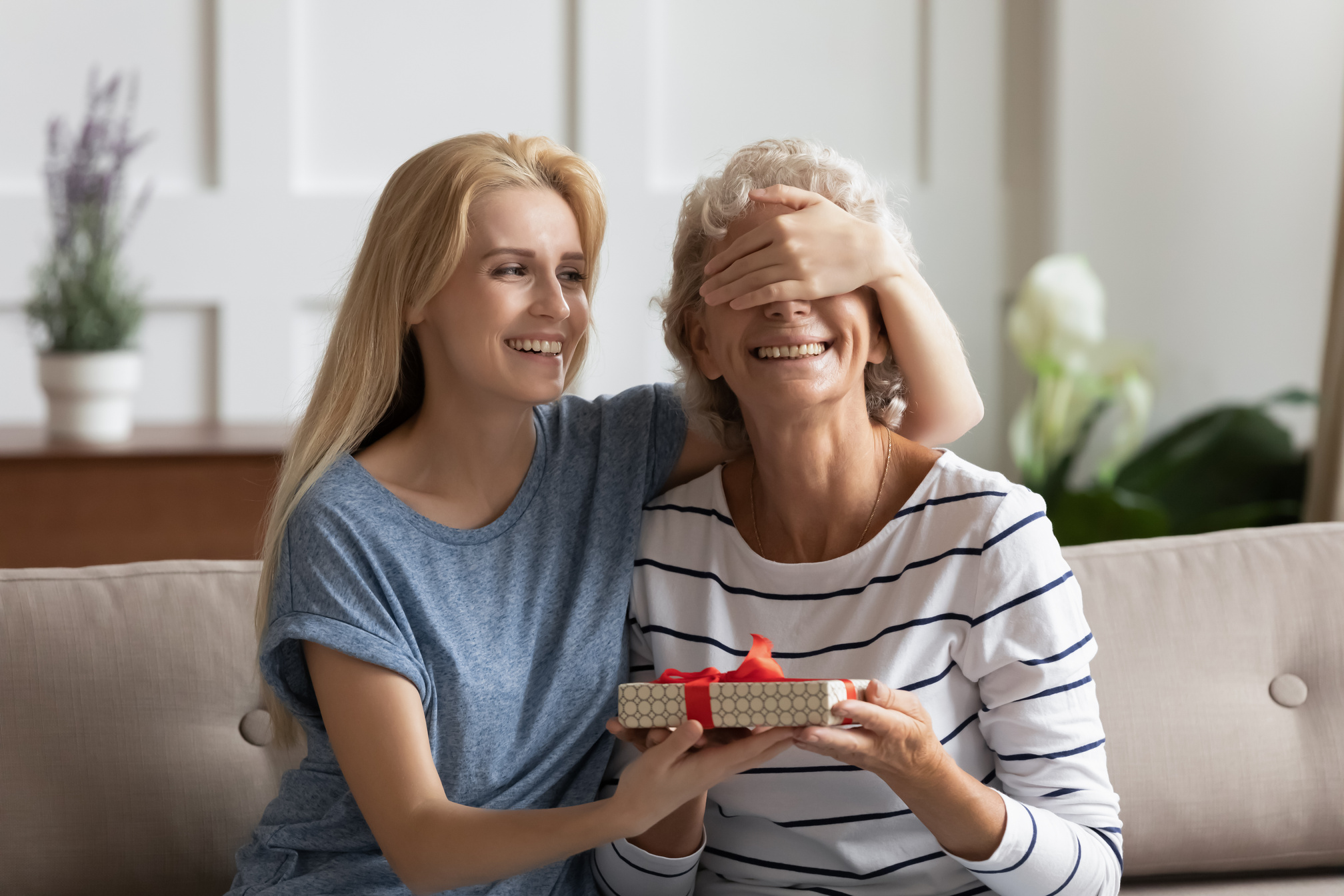 Grown up caring daughter making surprise gift for elderly mother